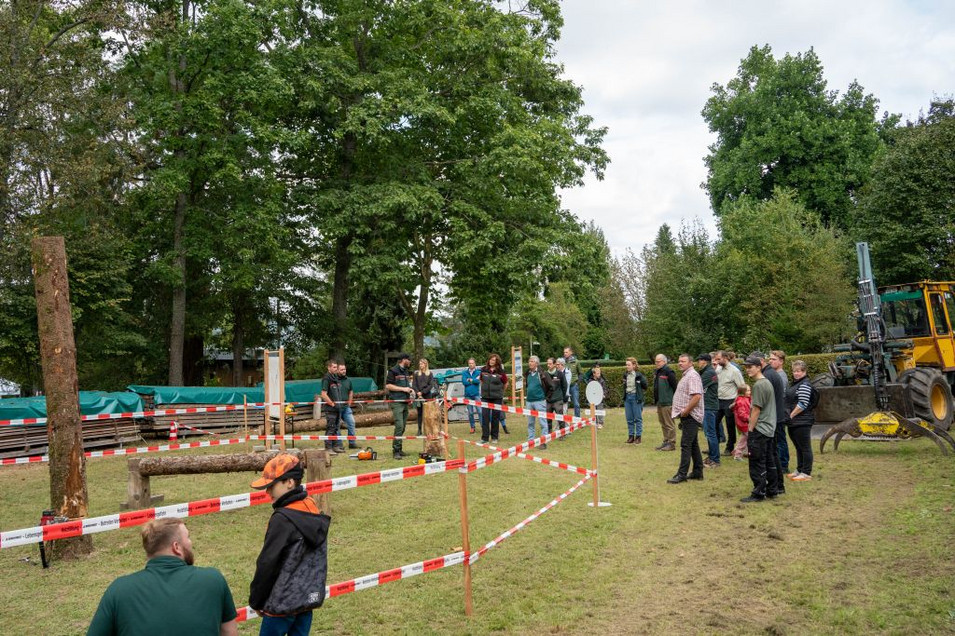 Das Bild zeigt Technikshow mit mehreren Menschen. In der Mitte eine abgesperrte Zone für die Vorführungen, im Hintergrund Holzrückemaschinen