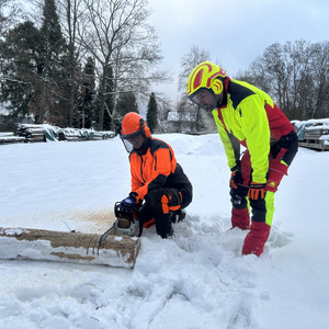 Motorsägen-Workshop Dieses Bild zeigt ein Frau mit einer Motorsäge und einen Mann im Schnee.