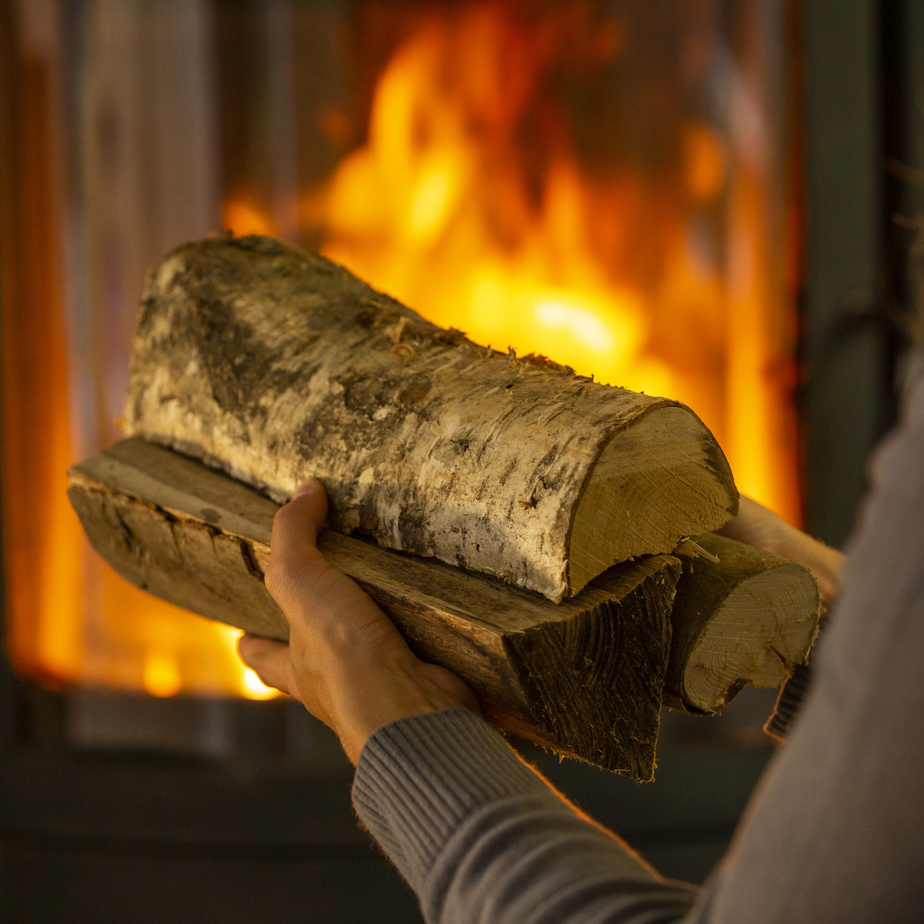 Heimeliges Kaminofenfeuer Das Bild zeigt: Hände mit Holzscheiten im Hintergrund ein Kaminofen