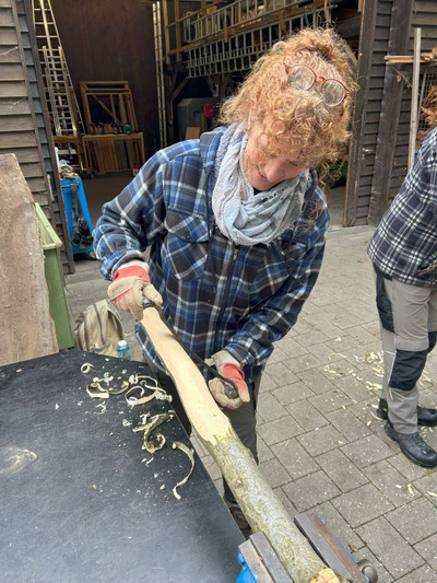 Eine Teilnehmerin entrindet ein Stück Holz zur weiteren Verarbeitung